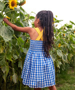Back of child wearing Frugi 100% organic cotton dress in blue and white gingham showing yellow shoulder straps and elasticated upper body