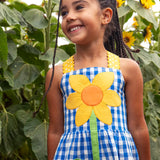 Close up of Child wearing Frugi 100% organic cotton dress in blue and white gingham showing a large sunflower patch on front 