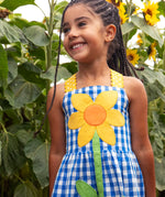 Close up of Child wearing Frugi 100% organic cotton dress in blue and white gingham showing a large sunflower patch on front 
