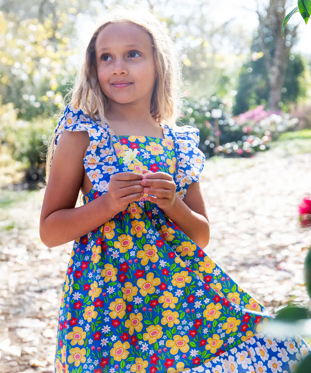 Child wearing Frugi 100% organic cotton Audrey dress in blue with a repeating floral design showing frill on shoulder straps