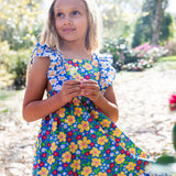 Child wearing Frugi 100% organic cotton Audrey dress in blue with a repeating floral design showing frill on shoulder straps