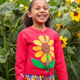 Child wearing Frugi 100% organic cotton Ella cardigan in pink with sunflower design on the front with tall sunflowers in the background