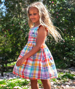 Side of child waering Frugi springtime dress in pastel check with hyacinth embroideries on the upper body with trees in the background