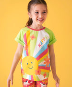 Child wearing Frugi 100% organic cotton light green raglan short sleeve t-shirt with a large happy sun print on the front against a orange background.