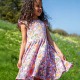 Child wearing Frugi's 100% organic cotton skater dress in violet purple with a repeating meadow inspired print on a grassy hill 