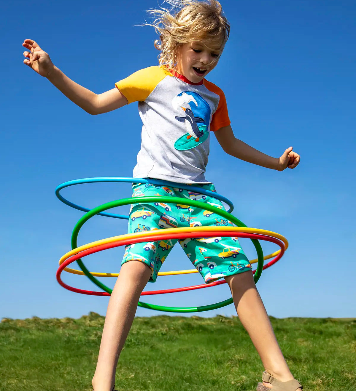 Child wearing Frugi 100% organic cotton shorts in light green with repeating beach theme vehicles. Child jumping in the air 