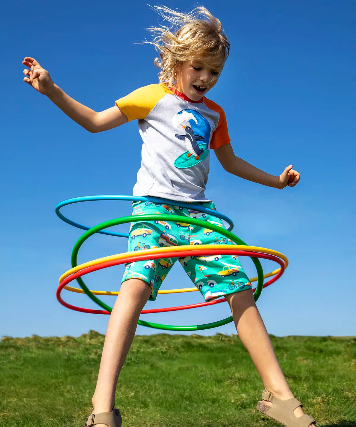 Child wearing Frugi 100% organic cotton shorts in light green with repeating beach theme vehicles. Child jumping in the air 