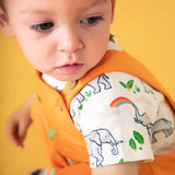 Baby wearing Frugi's 100% organic cotton body suit in white with a repeating elephant print against a orange background
