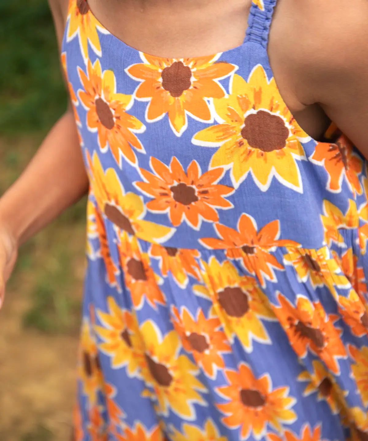 Close up of child wearing Frugi 100% organic cotton Sophie summer sleeveless dress in purple with a repeating sunflower print