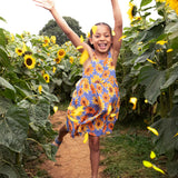 Child wearing Frugi 100% organic cotton Sophie summer sleeveless dress in purple with a repeating sunflower print in a sunflower field