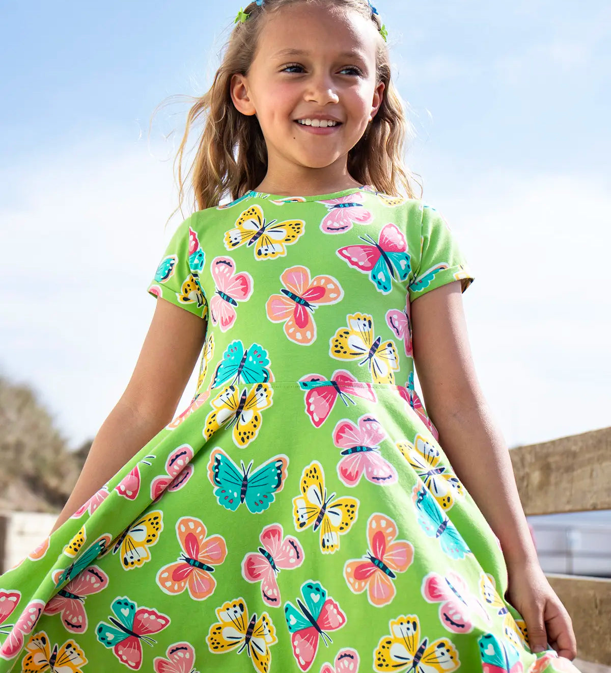 Child wearing Frugi 100% organic cotton spring skater dress in green with a repeating colourful butterfly print.