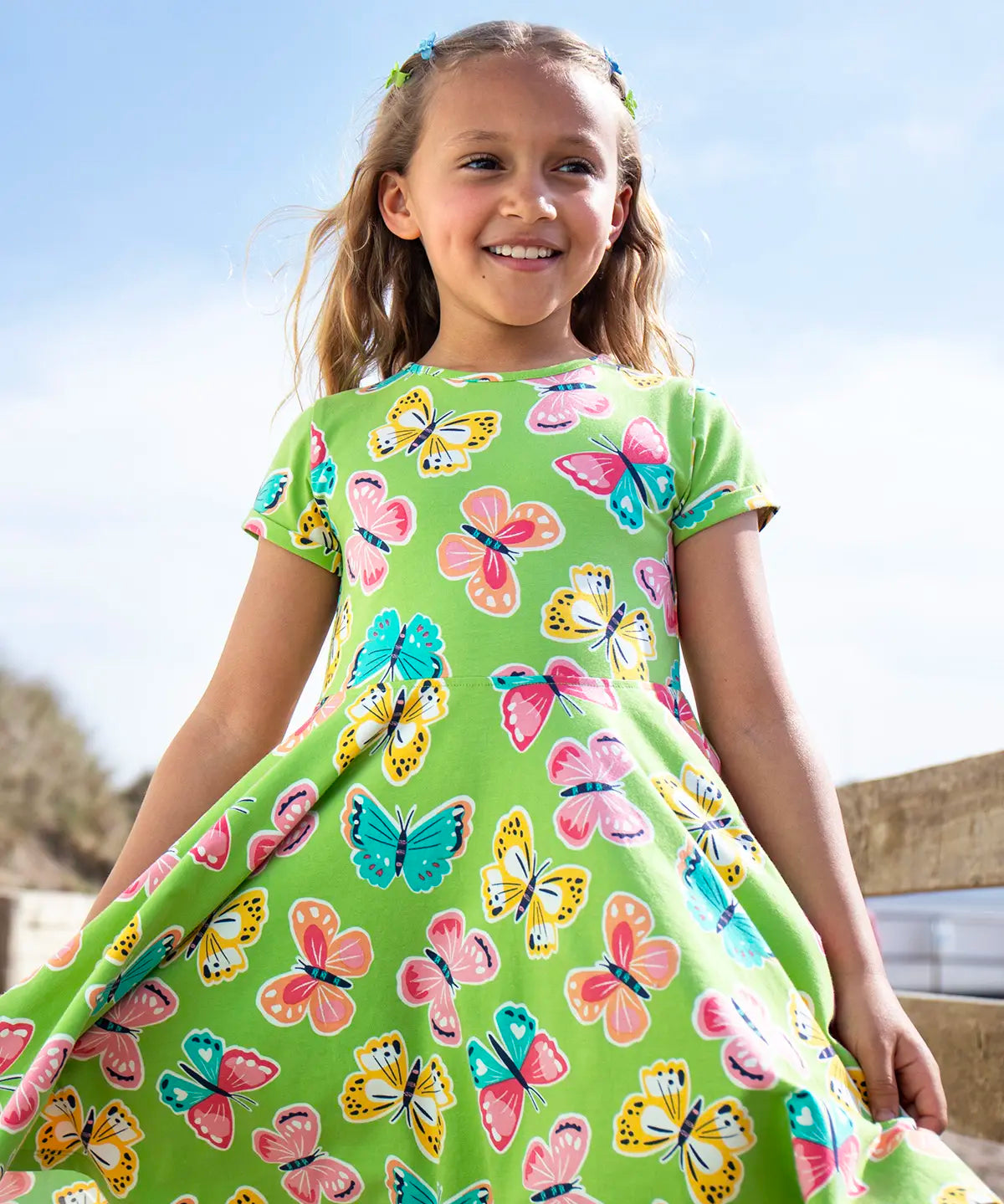 Child wearing Frugi 100% organic cotton spring skater dress in green with a repeating colourful butterfly print.