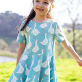 Child wearing Frugi's 100% organic cotton sunshine skater dress in light blue with a repeating white goose print in a field