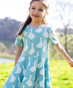 Child wearing Frugi's 100% organic cotton sunshine skater dress in light blue with a repeating white goose print in a field