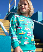 Child wearing Frugi 100% organic cotton sweatshirt in light green with repeating beach inspired vehicles. Child on concrete stairs
