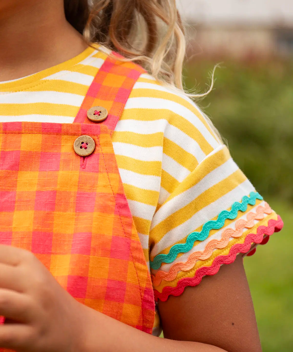 Close up of Child wearing Frugi 100% organic cotton yellow and white striped t-shirt showing the ric rac decorative trim 
