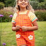 Child wearing Frugi 100% organic cotton Thea yellow and white striped t-shirt with a ric rac decorative trim with dungarees in a grassy field