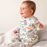 Baby wearing Frugi's 100% organic cotton kimono style babygrow in white with a repeating elephant and rainbow print on a grey blanket