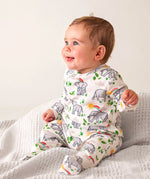 Baby wearing Frugi's 100% organic cotton kimono style babygrow in white with a repeating elephant and rainbow print on a grey blanket