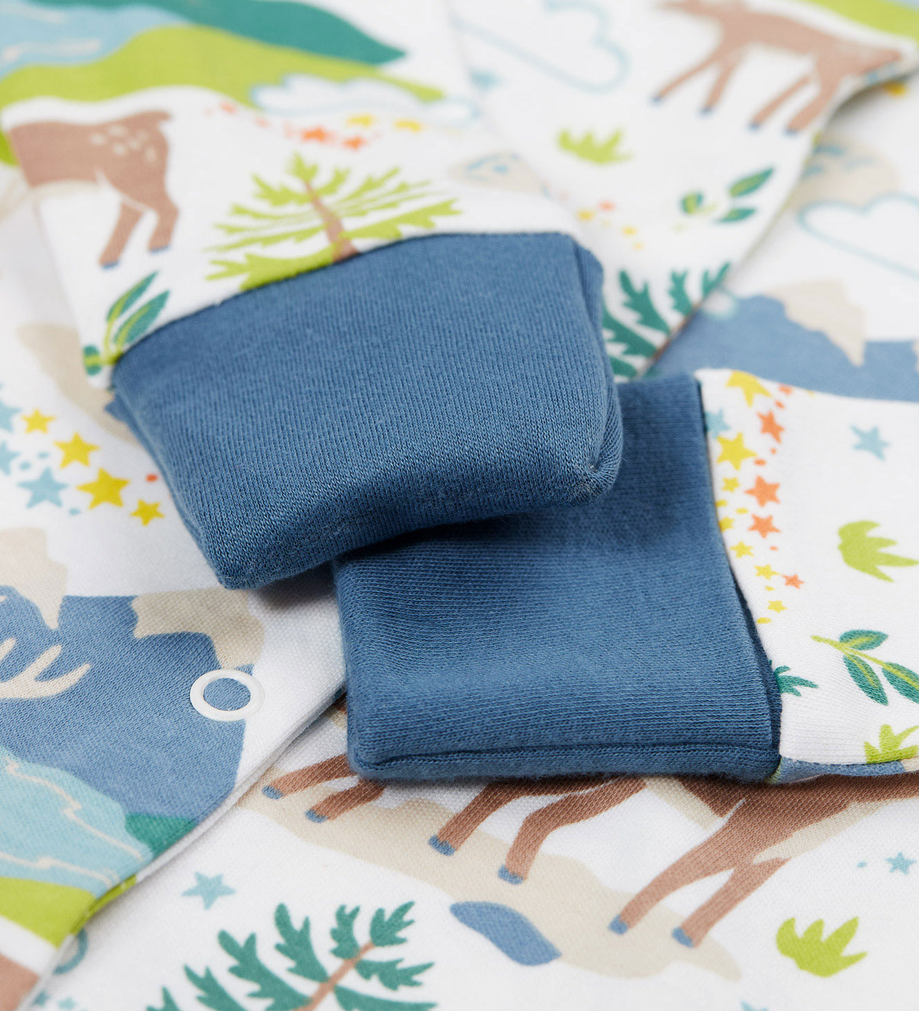 A close up of the navy coloured cuffs that can fold over in place of scratch mitts on the A Frugi Caribou Fields Organic Cotton Lovely Babygrow. A white babygrow with a reindeer themed print with green and blue details. This babygrow is a part of a wide range of organic cotton clothing for children available here at Babipur. 