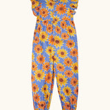 Frugi Lowenna jumpsuit in purple with a repeating sunflower print. Showing frilled shoulder and elasticated leg cuffs