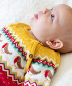 A baby wearing the Frugi lumi knitted festive romper fair isle available at Babipur. A GOTS organic cotton soft knitted all in one in a fairisle design with robins. Features button fasteners running down from the shoulder.