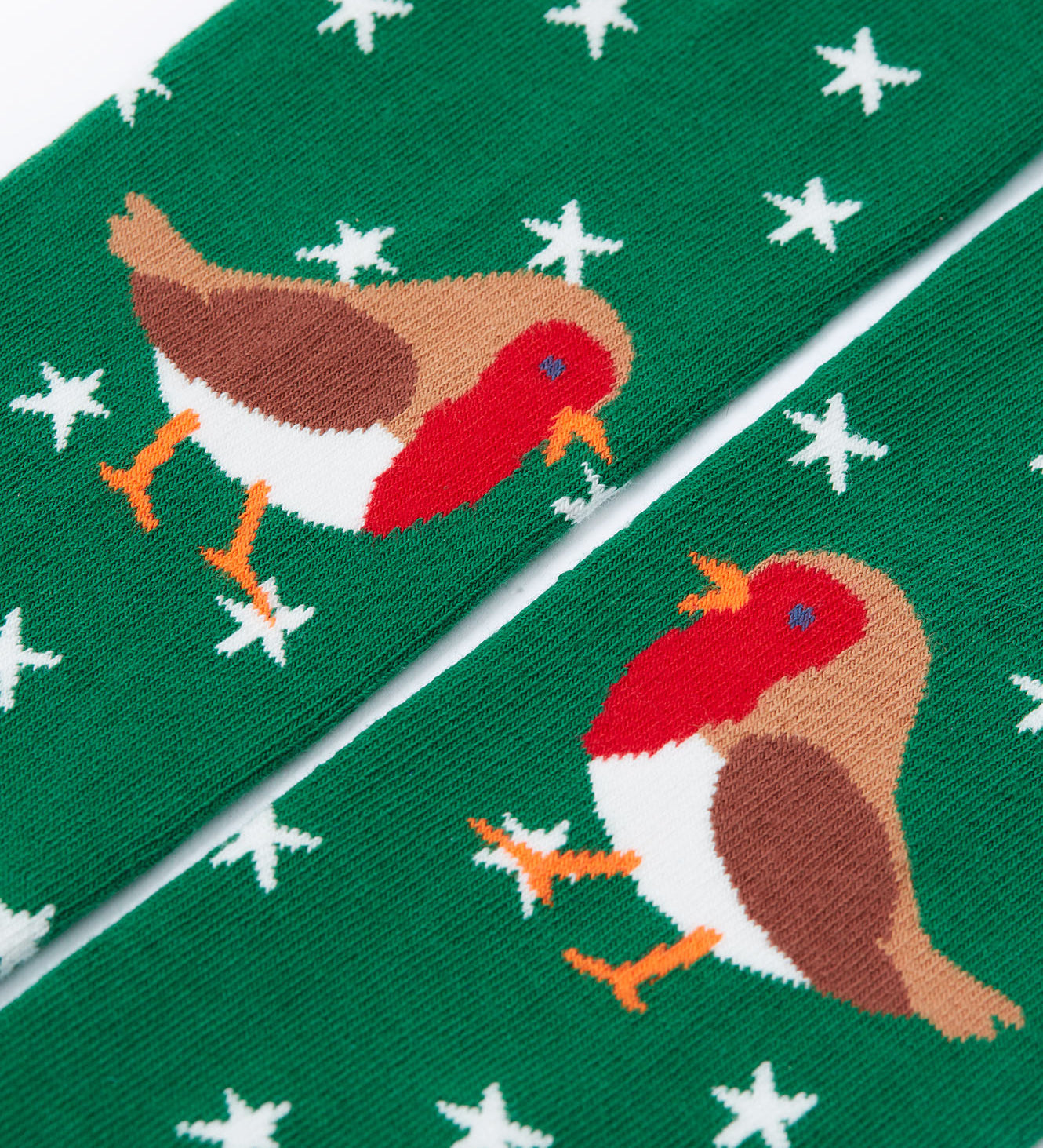 A close up of the robin details on the green pair of norah tights from the. Frugi Norah tights in green robin and berry red 2 pack available at Babipur. A pair of GOTS organic cotton tights in green with white stars and a robin design. Other pair is a bright festive red.
