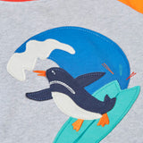 Close up of the Frugi 100% organic cotton short sleeve t-shirt in grey  Showing a surfing penguin patch on the front