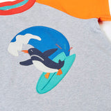 Frugi 100% organic cotton short sleeve t-shirt in grey laid flat showing orange sleeve and a surfing penguin patch 