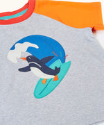 Frugi 100% organic cotton short sleeve t-shirt in grey laid flat showing orange sleeve and a surfing penguin patch 