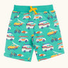 Frugi 100% organic cotton shorts in light green with repeating beach theme vehicles. Shows side pockets and yellow waist tie