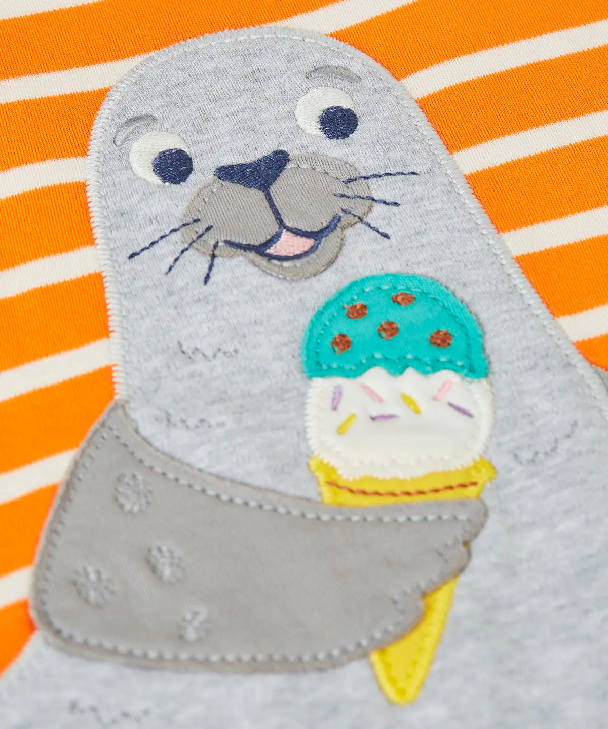 Close up of the playful seal patch on the Frugi 100% organic cotton short sleeve t-shirt in orange and white stripes 