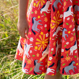 Close up of child wearing Child wearing Frugi 100% spring skater dress in coral pink with repeating horses and  showing the frill on the hem  