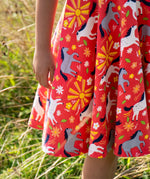Close up of child wearing Child wearing Frugi 100% spring skater dress in coral pink with repeating horses and  showing the frill on the hem  