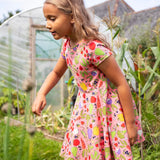 Child wearing Frugi's 100% organic cotton spring skater dress in pink with a repeating fruit and veg print in a garden