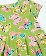 Frugi 100% organic cotton spring skater dress in green laid flat showing the repeating colourful butterfly print.