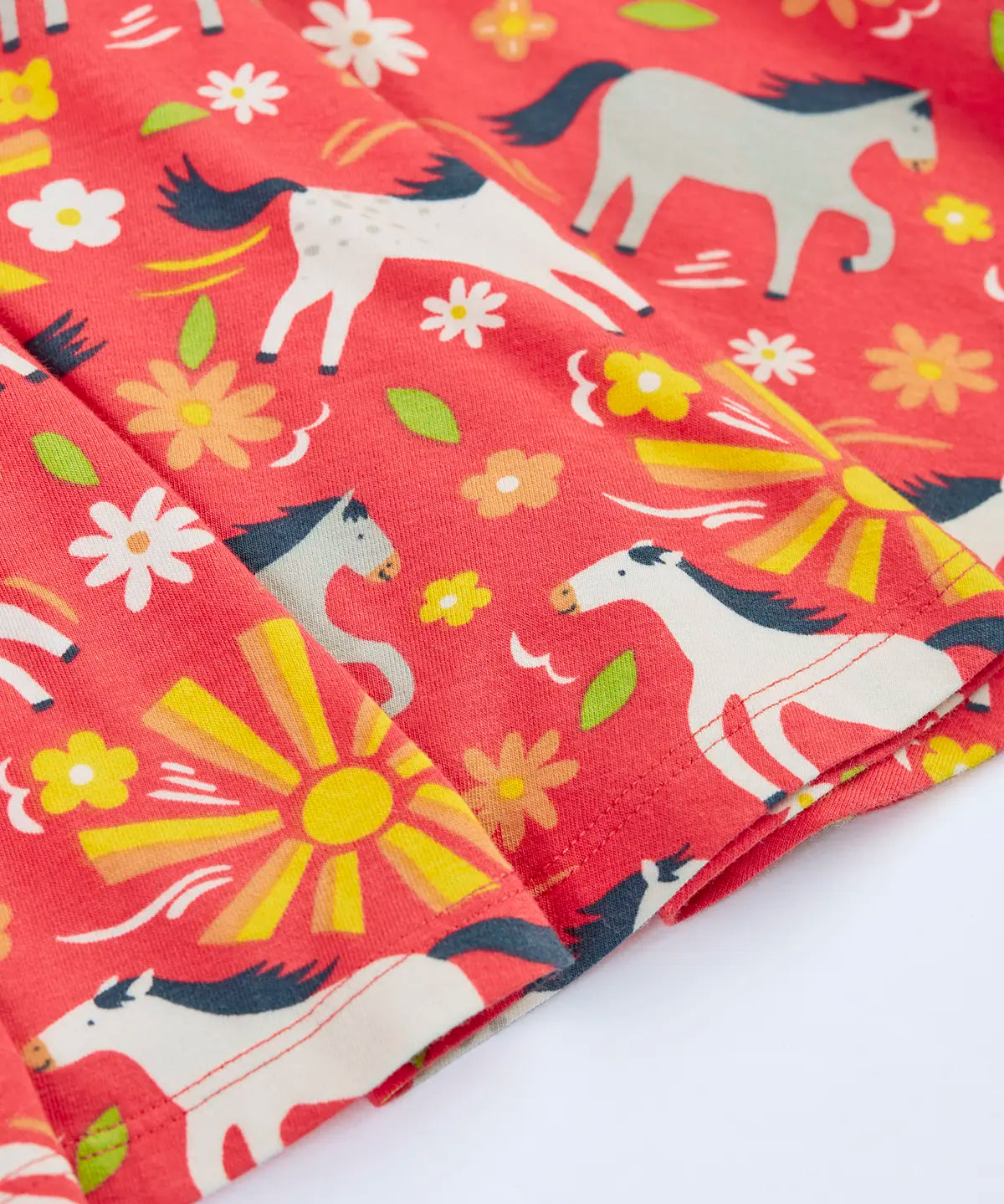 Close up of the repeating prints of white and grey horses on the Frugi 100% spring skater dress in coral pink