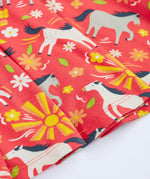 Close up of the repeating prints of white and grey horses on the Frugi 100% spring skater dress in coral pink