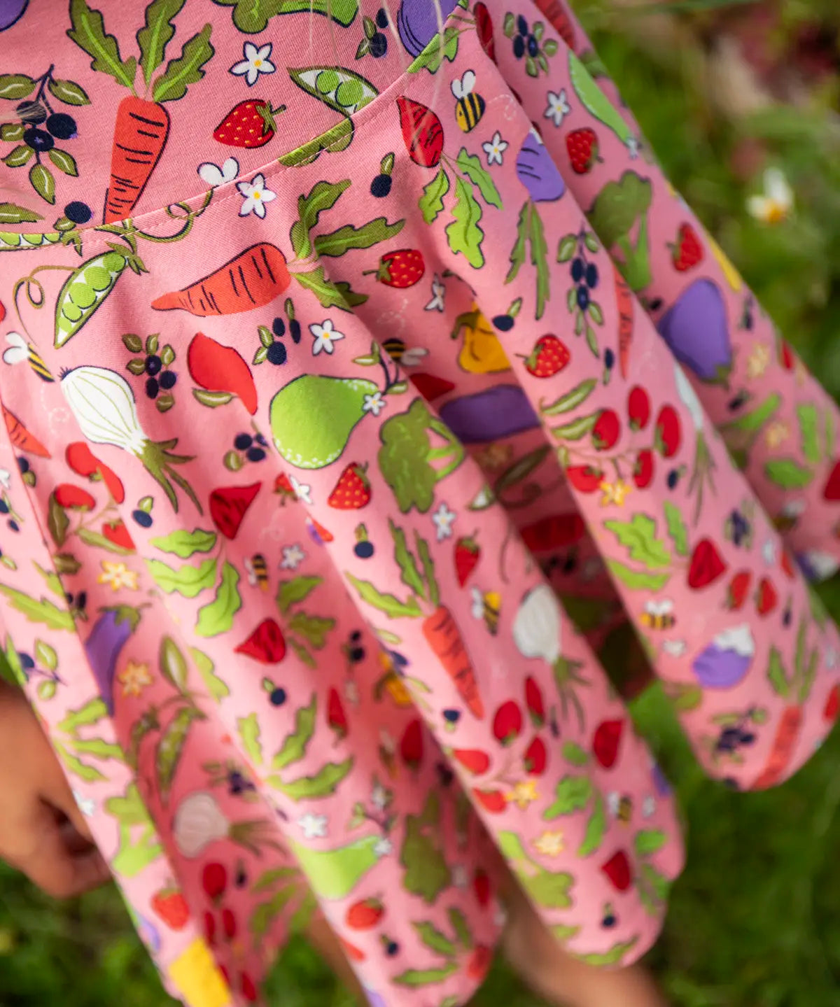 Close up of child wearing Frugi's 100% organic cotton spring skater dress in pink showing repeating fruit and veg print 