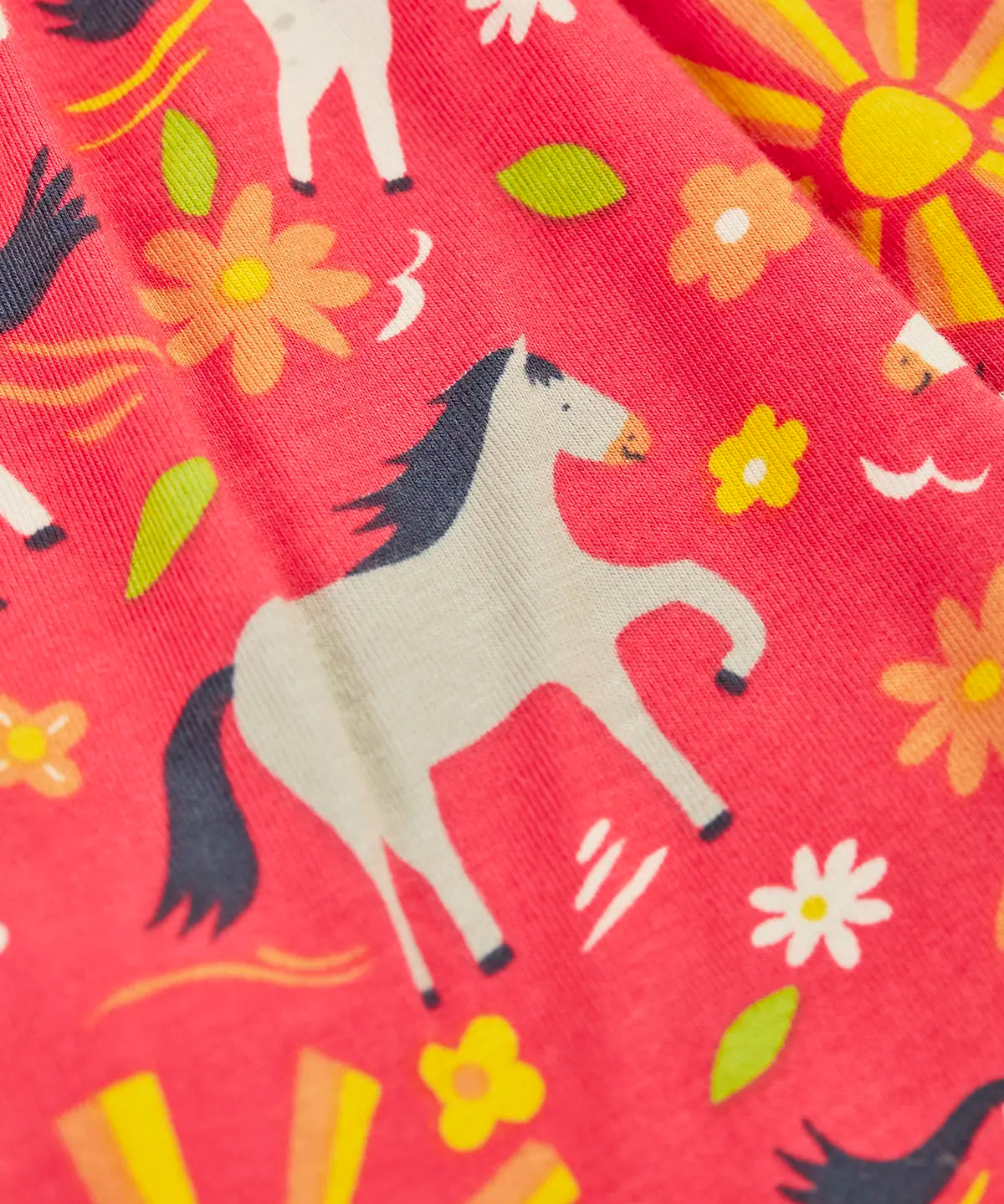 Close up of the repeating pony print on the Frugi 100% organic cotton spring skort in coral pink 