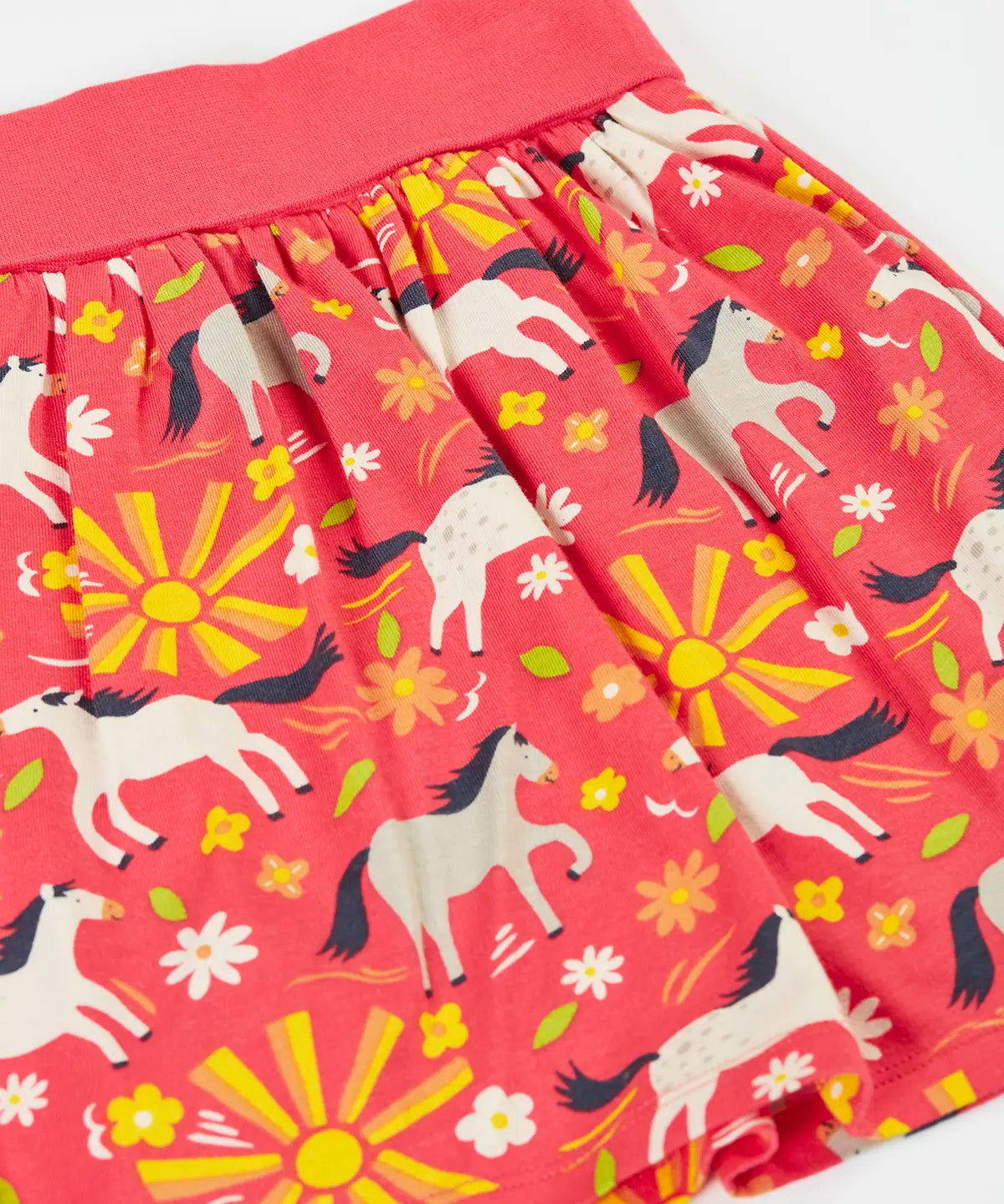 Frugi  spring skort in coral pink laid flat showing the repeating white and grey pony and sunshine print.