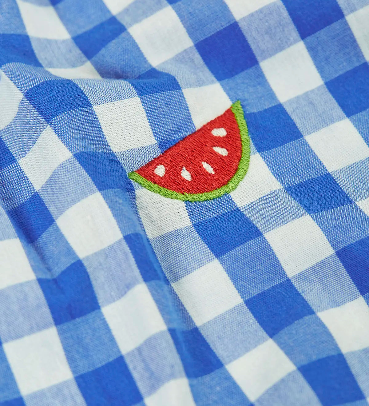 Close up of Frugi 100% organic cotton summer short dungarees in blue and white gingham showing a watermelon embroidery 