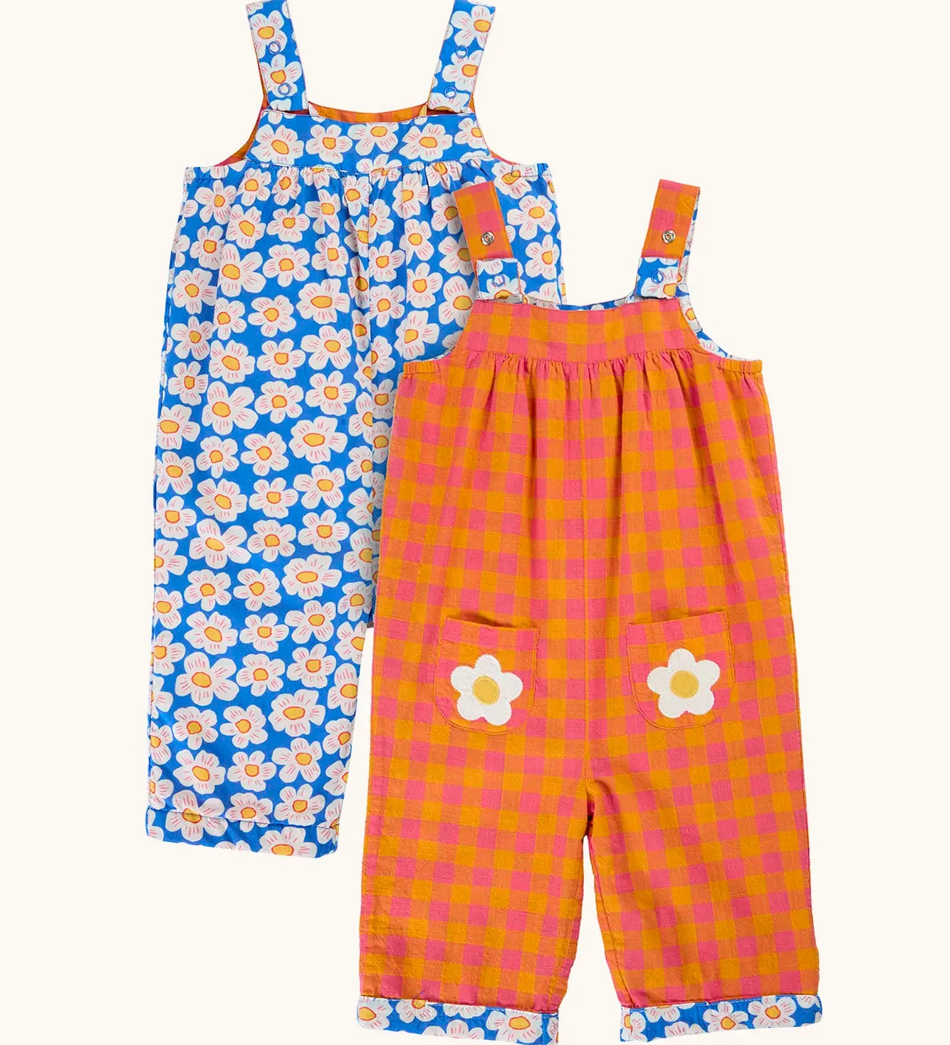 Frugi 100% organic cotton Sylvie reversible dungarees showing a blue with repeating daisy design and a orange and pink check design on reverse side