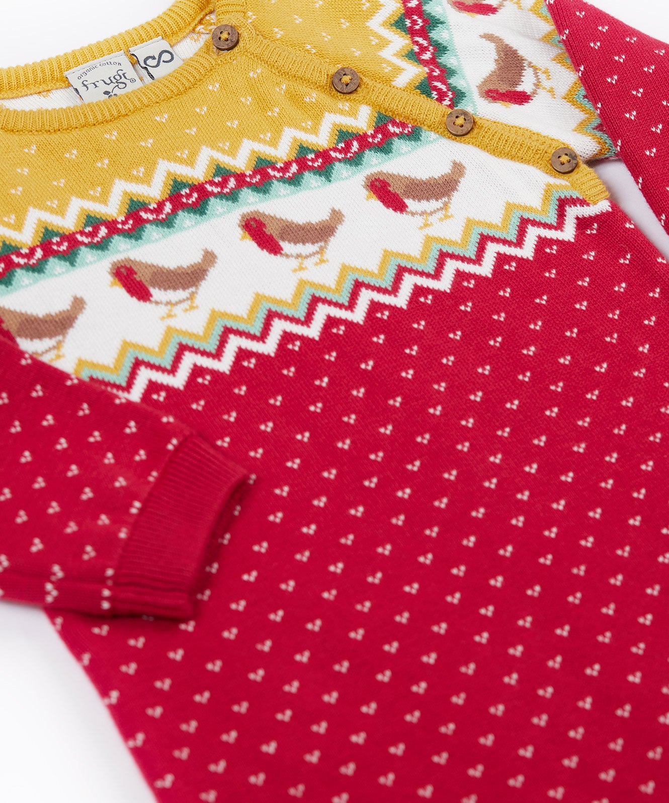 A close up of the Frugi lumi knitted festive romper fair isle available at Babipur. A GOTS organic cotton soft knitted all in one in a fairisle design with robins. Features button fasteners running down from the shoulder.