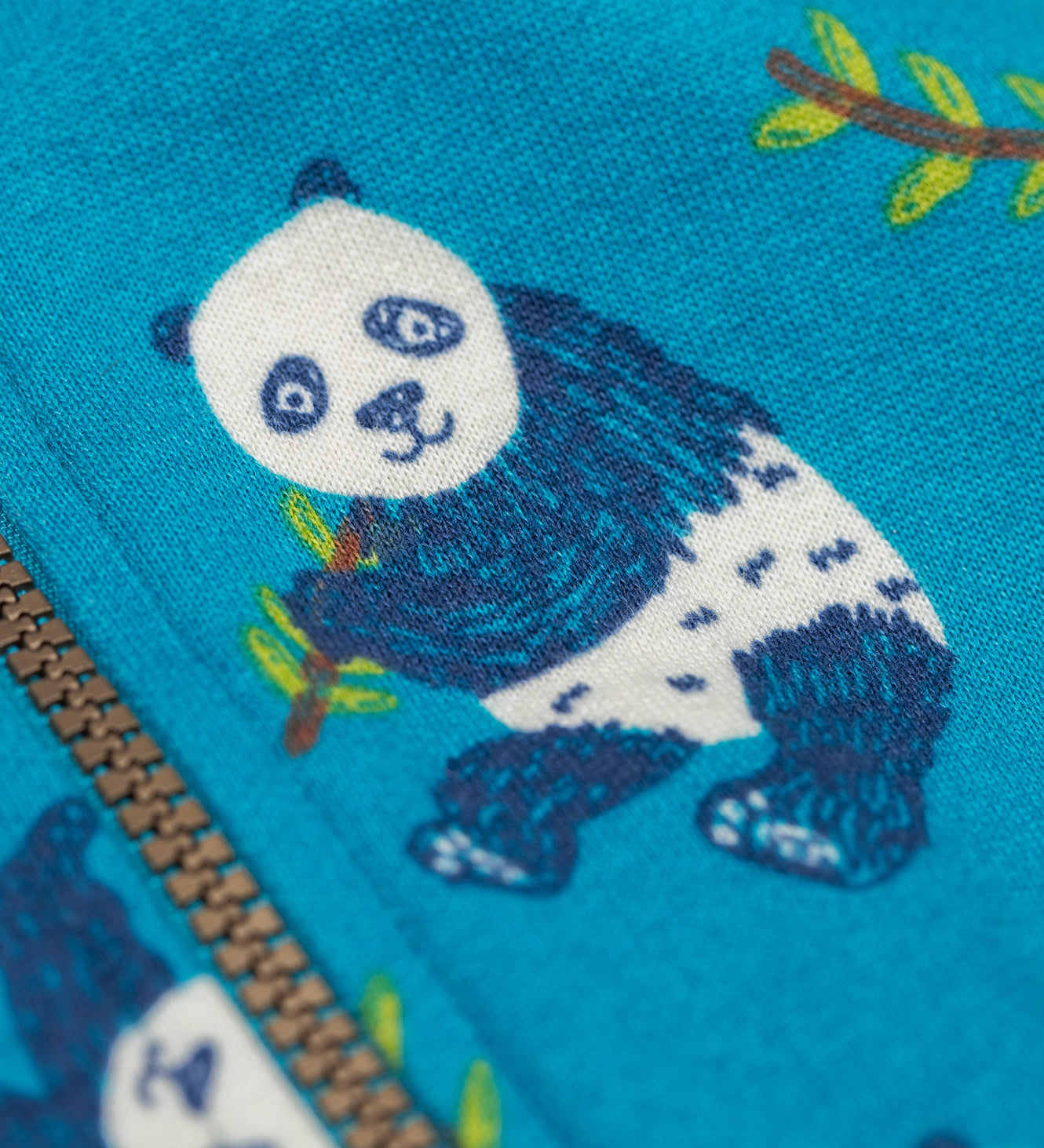 A close up of a panda fearured on teh print on the Frugi snuggle suit in panda pals available at Babipur. A GOTS organic cotton light blue hooded all in one with a playful panda design. Features a full length zip fastener.