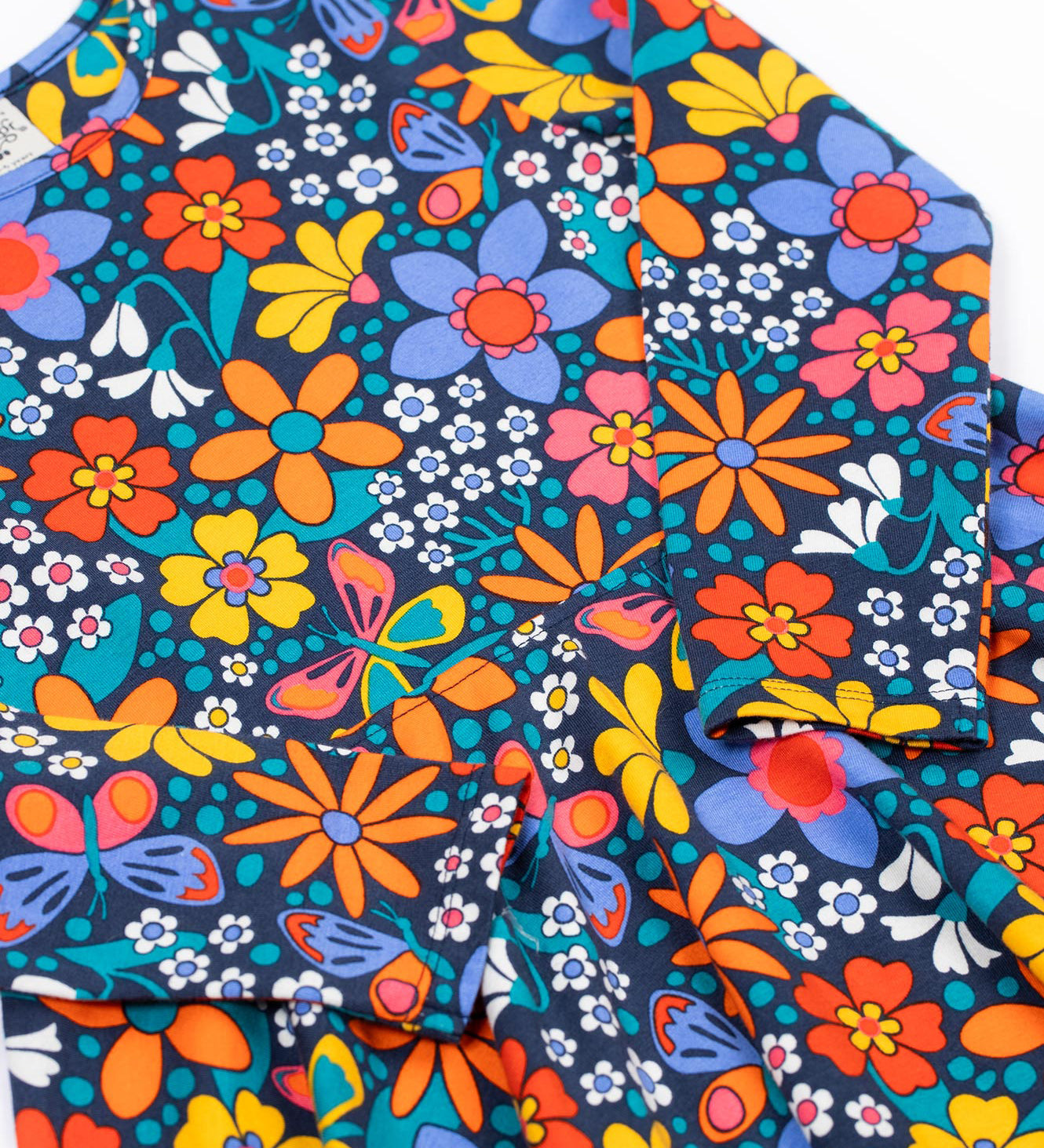 A close up of the Frugi sofia skater dress in navy / retro flowers available at Babipur. A GOTS organic cotton skater dress in navy with a bright retro floral design. 