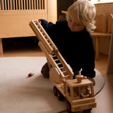 Child playing with the Fagus fire engine wooden toy with a rotating 3-piece extendable ladder, working steering, rubber wheels and 6 peg doll figures.