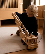 Child playing with the Fagus fire engine wooden toy with a rotating 3-piece extendable ladder, working steering, rubber wheels and 6 peg doll figures.