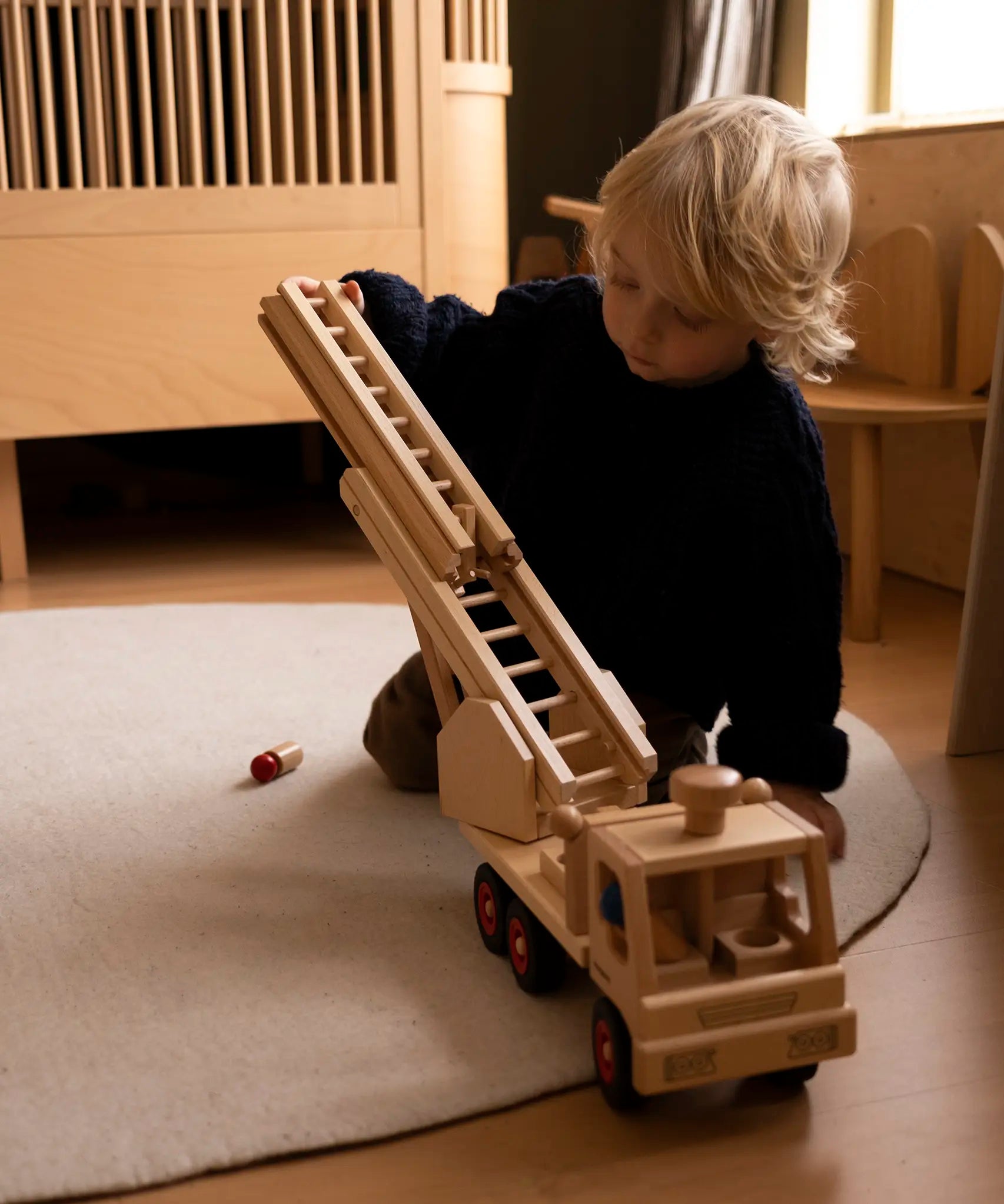 Child playing with the Fagus fire engine wooden toy with a rotating 3-piece extendable ladder, working steering, rubber wheels and 6 peg doll figures.
