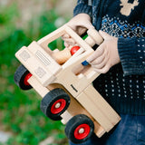 Classic wooden unimog truck by Fagus with peg dolls, carried by child outside.